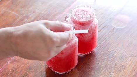 manos agitando bebidas de sandía en una mesa de madera