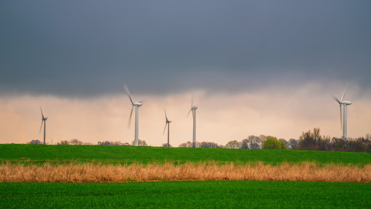 Timelapse of wind turbines rotating against stormy, dramatic skies over green fields near the East Frisian Islands, Lower Saxony, Germany.