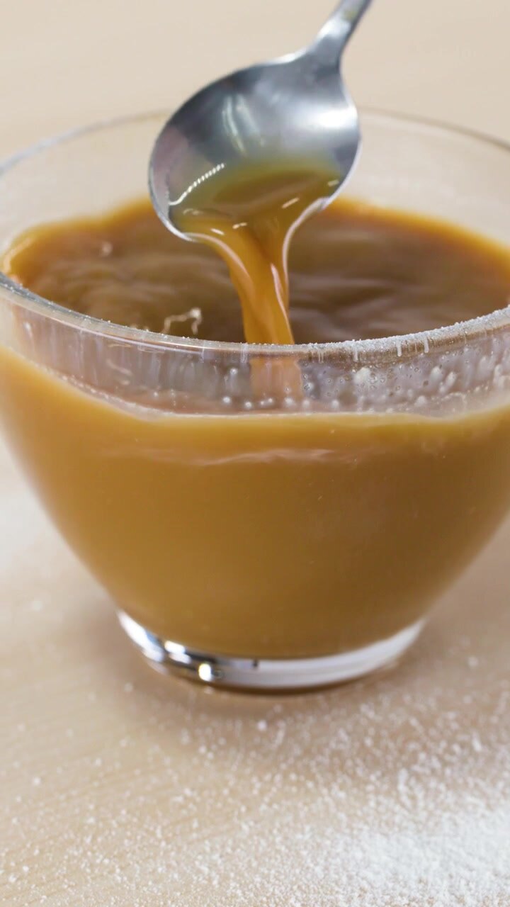 Close-up of a spoon stirring hot coffee with milk in a glass mug on table.
