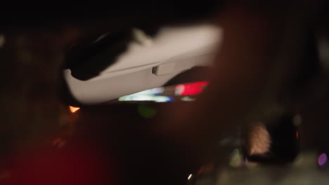 first-person view of a woman's face reflected in the car mirror at night. the blurred city lights create a dreamy atmosphere. shot with a handheld camera