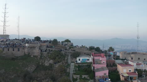 People-visiting-historic-hilltop-Bunkers-del-Carmel-with-panoramic-views-over-city.-Pull-back-shot-of-hill-and-Turo-de-la-Rovira-park.-Barcelona,-Spain