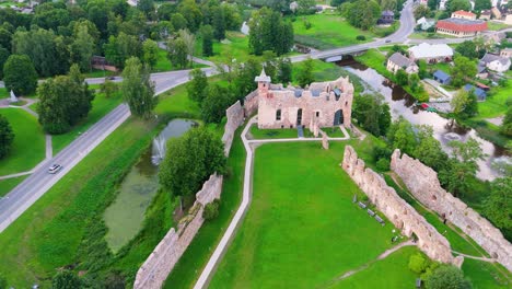 aerial view of dobele castle ruins, flowing berze river and illuminated fountains at sunset serene latvian summer evening from above, scenic aerial of latvian historical landscape in golden hour