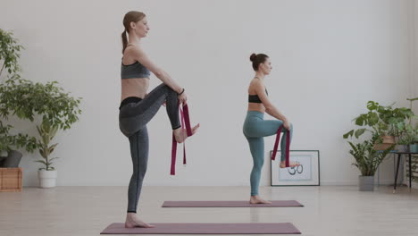 dos mujeres jóvenes usando cinturones de yoga durante el entrenamiento