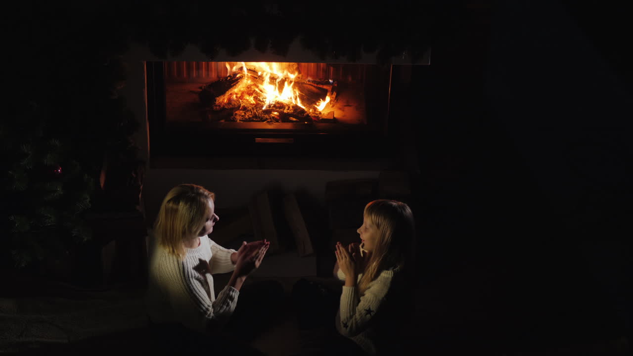 엄마와 딸은 저녁에 아늑한 따뜻한 집에서 벽난로 옆에서 놀고 있습니다.
