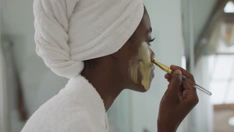 portrait of african american attractive woman applying face mask in bathroom