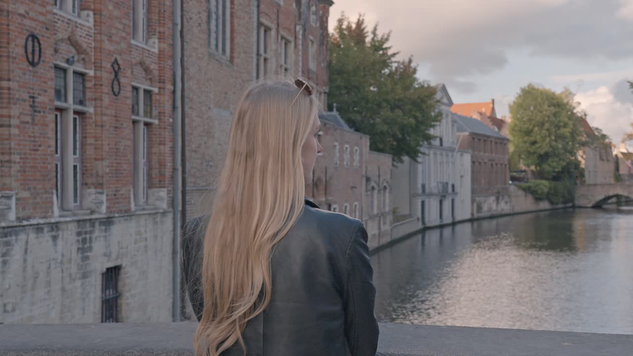 Woman, viewed from behind, looking at the canal at sunset in Blinde-Ezelbrug (Blind Donkey Bridge) in Bruges, Belgium