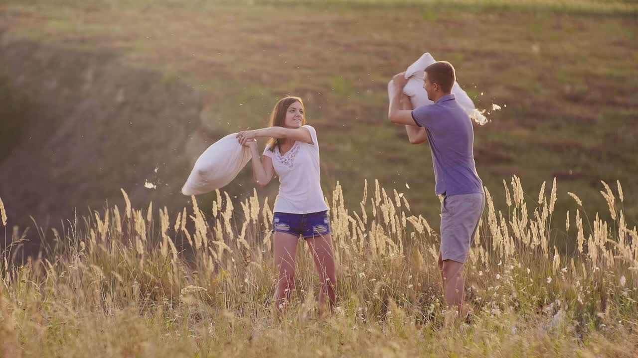 젊은 사람들은 미친 듯이 즐겁게 지내고 있다 한 여자는 친구와 함께 베개를 때리고 있다 깃털이 날고 있다