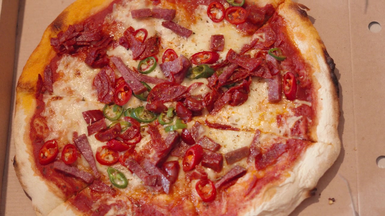 Vista dall'alto di pizza di carne piccante con pepperoni, salame e peperoncini in cartone da asporto.