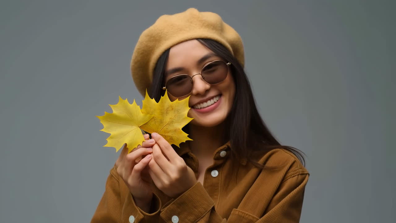 Giovane donna asiatica che sorride e tiene in mano foglie d'acero gialle