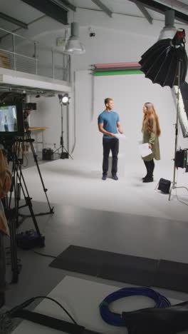 vertical video of actors with scripts in rehearsal shooting movie or video in studio with female director and film crew and watching on monitor