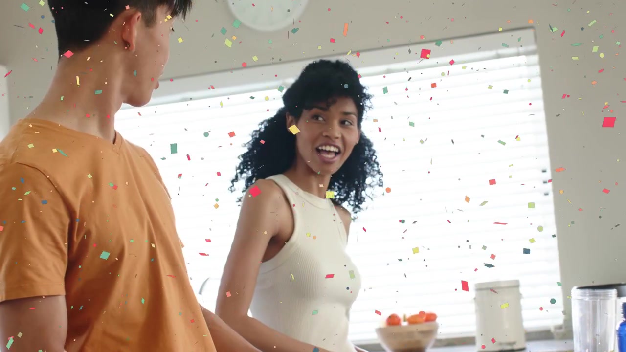 Couple prepping food at home on boards, woman smiling and speaking causing man glancing, confetti
