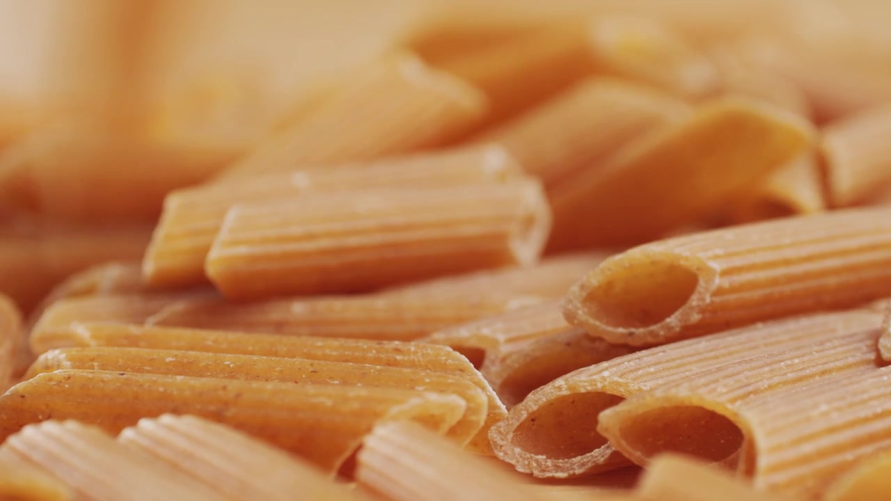 Pasta integrale biologica, maccheroni di semola di grano duro, penne rigate crude in una ciotola di legno. Filmato 4k di alta qualità