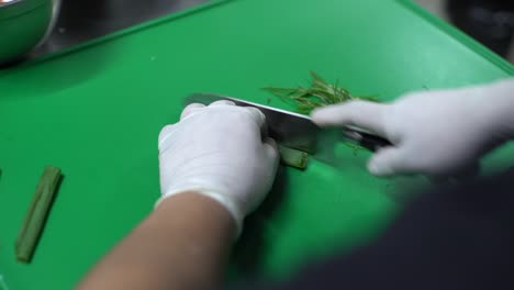 Chef-hands-cutting-green-onion-on-green-cutting-board,-top-view