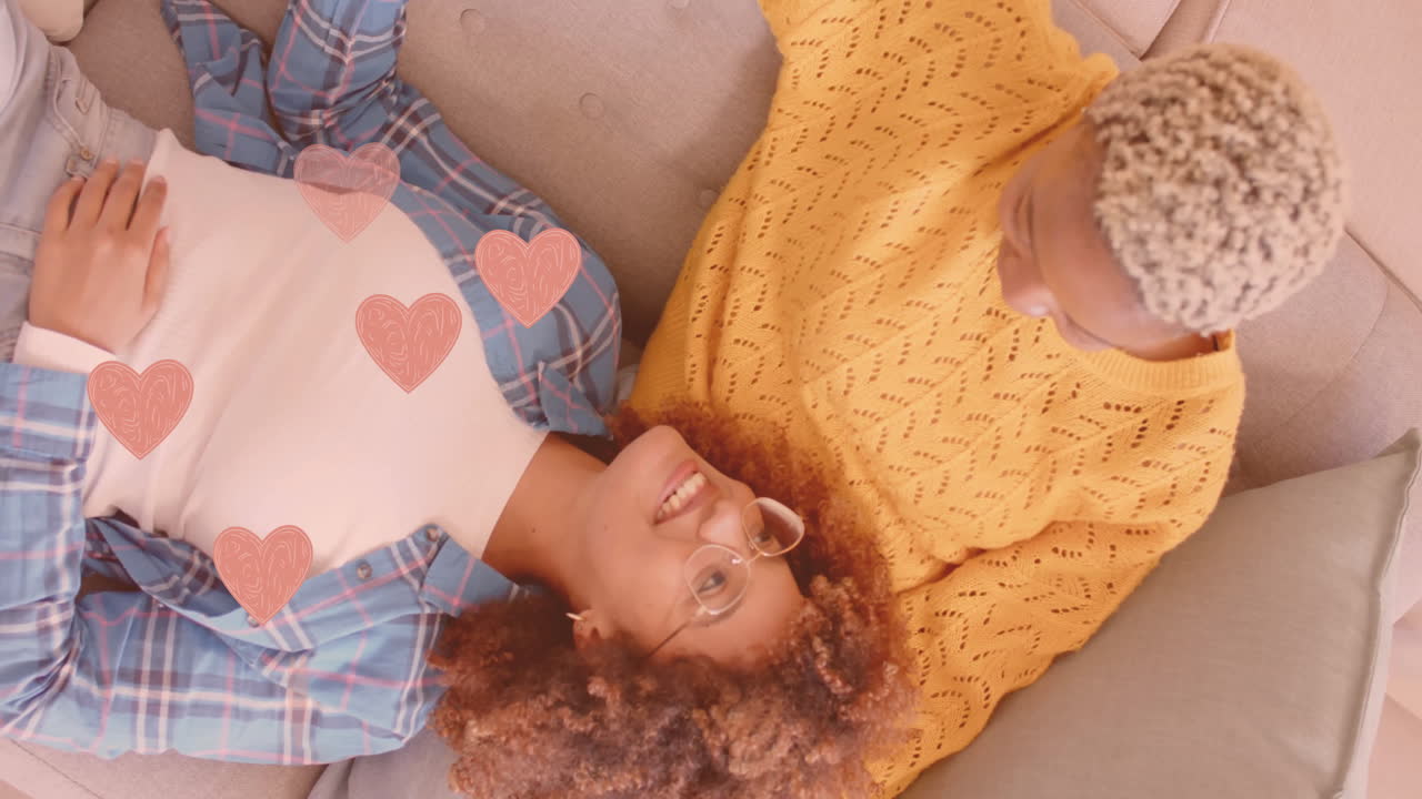 animación de los corazones sobre feliz pareja diversa en el sofá en casa