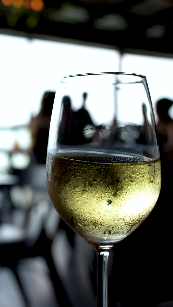 Primo piano di un bicchiere da vino coperto di condensa in un bar all'aperto con avventori sfocati sullo sfondo.