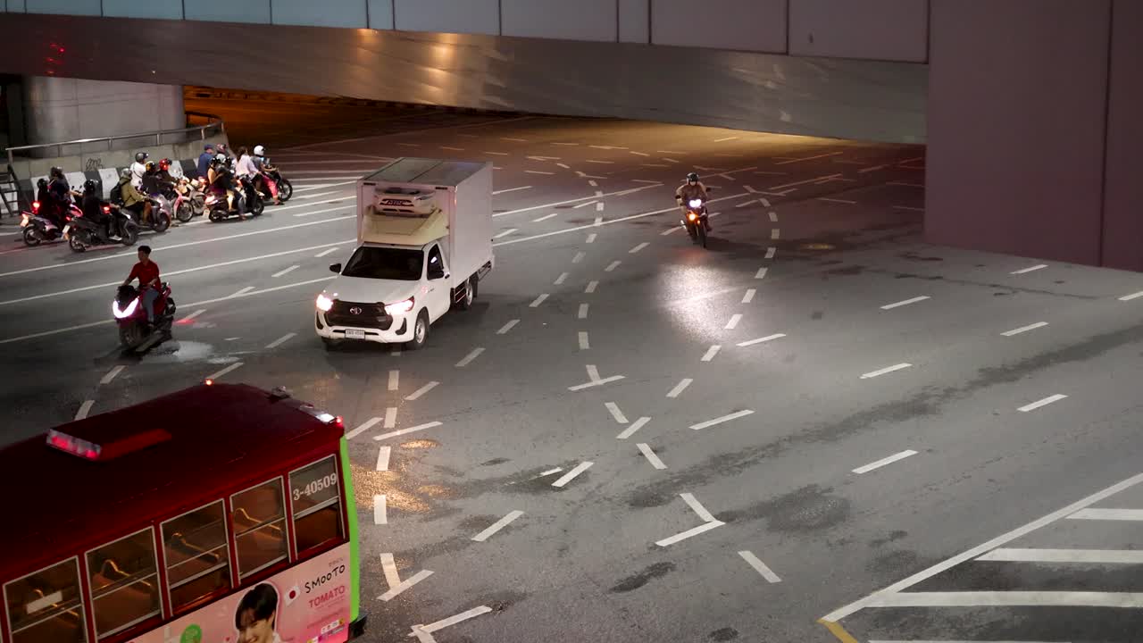 Overhead view of bus, truck, and motorbikes navigating wet Sathorn Road at night, Bangkok