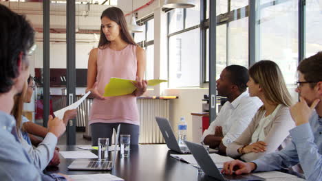 Female-manager-hands-out-document-and-addresses-team-meeting