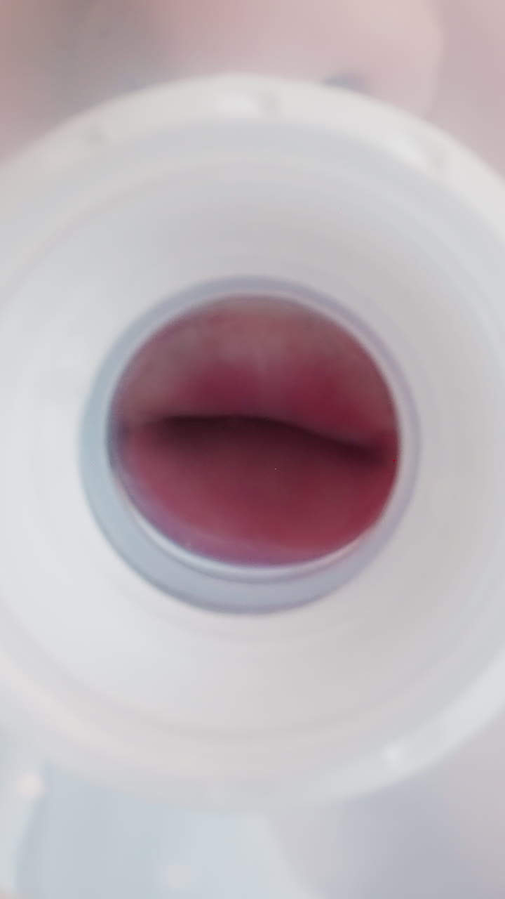 Boy holds nipple from baby bottle with lips standing in room. Toddler trying to drink from empty plastic bottle at home. View from bottom macro