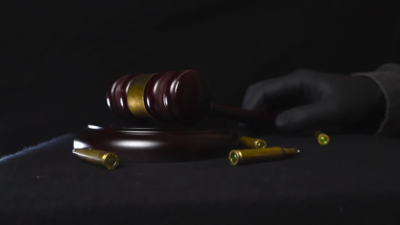 Brown wooden court gavel or hammer hit on a wooden board in slow motion while high caliber golden bronze bullets around fly into the air from the impact and fall down. black gloved hand swinging it