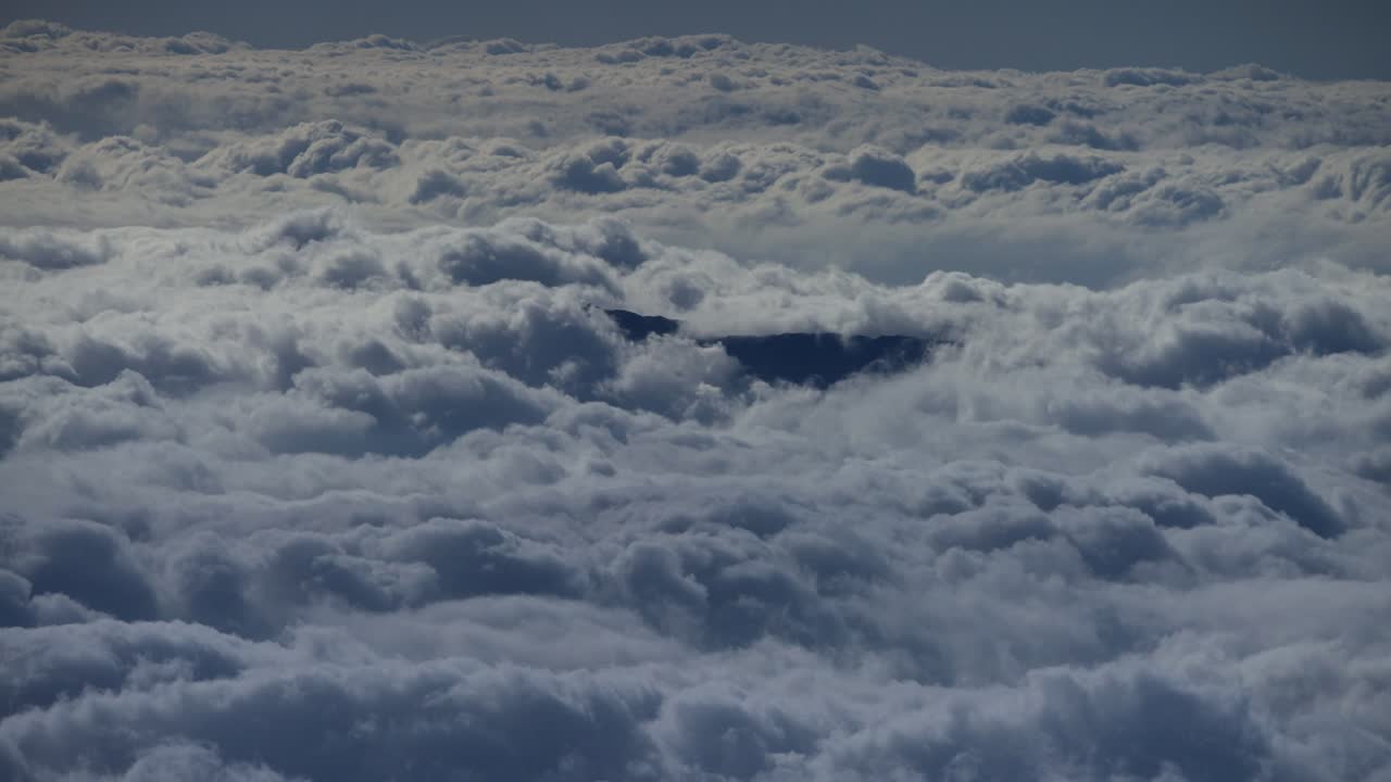 Wide aerial timelapse of fluffy clouds moving by dark mountain top