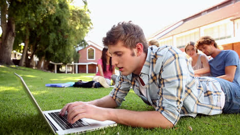 estudiante usando una computadora portátil con compañeros de clase sentados detrás en la hierba