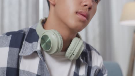 close up of upset asian teen boy with headphones stopping playing smartphone while sitting on sofa in the living room at home