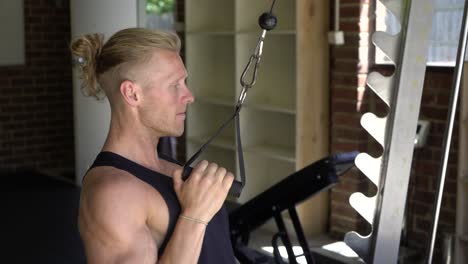 tattoo man muscles in home gym doing single arm lat pulldown shot from side