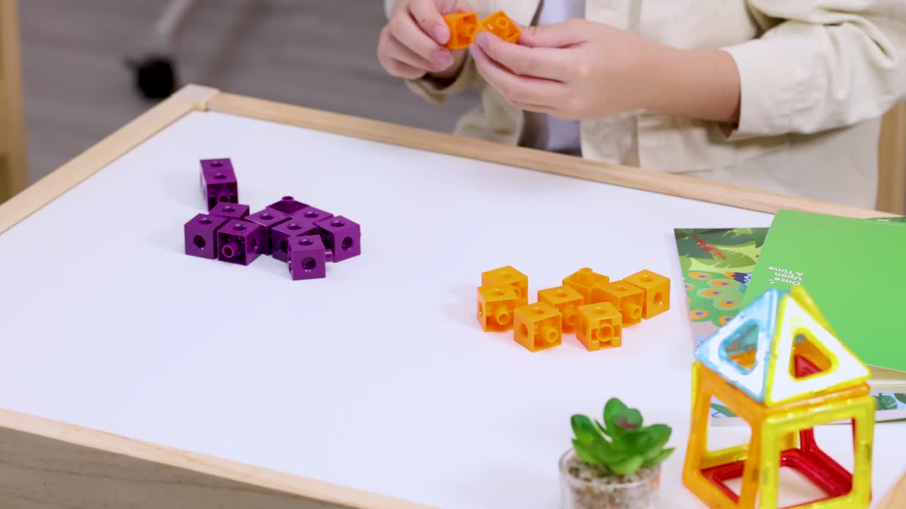 Child arranges colorful counting cubes on white table with educational toys, bright soft lighting