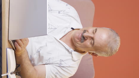 Vertical-video-of-Old-man-looking-at-laptop-making-positive-gesture.