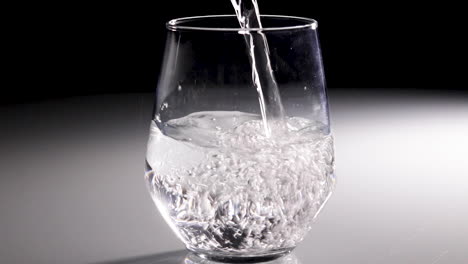 water being poured into a clear glass with a dark background