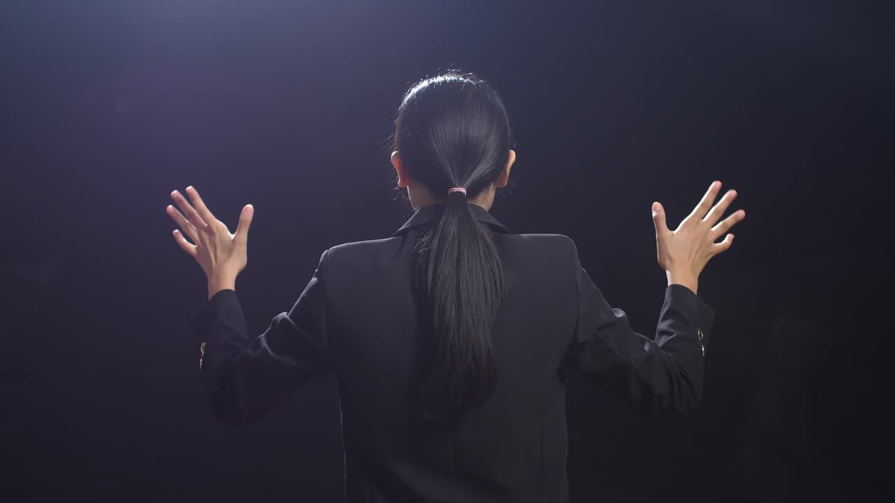 블랙 스크린 스튜디오 에서 연설 하는 동안 손 을 고 있는 비즈니스 슈트 를 입은 아시아어 연설자 의 뒷면