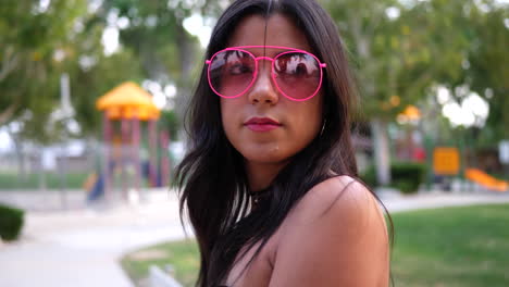 una joven hipster con ropa de moda vintage y gafas de sol de aviador rosa retro en un parque infantil a cámara lenta