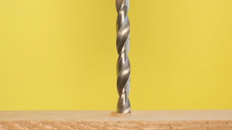 a metal drill makes a hole in a tree on a bright yellow background a metal drill makes a hole in a tree on a bright yellow background work with wood for the manufacture of furniture