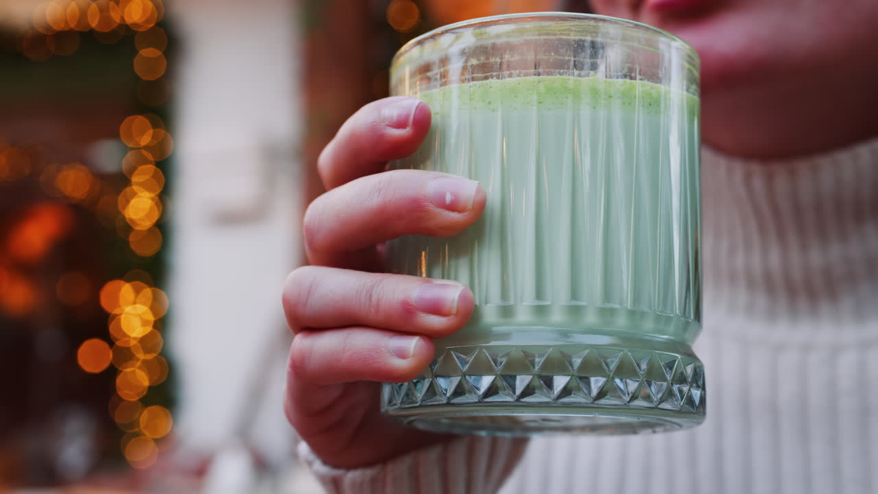 Close up of a woman drinking a matcha latte with a paper straw at a cafe