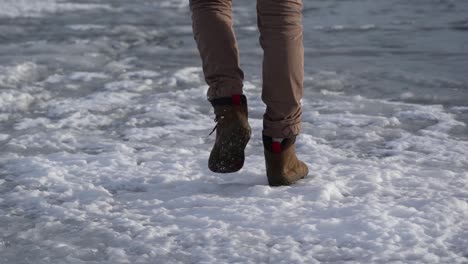 Close-view-of-the-boots-of-a-man-walking-on-ice-in-slow-motion