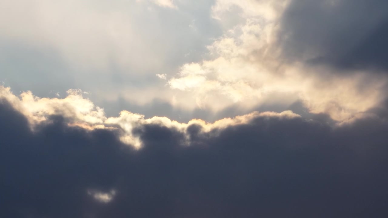 Sun breaking through dramatic dark storm clouds casting golden light rays at dusk