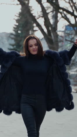 attractive girl posing on camera in the city park. beautiful model in black clothing walking outdoors. lovely girl with opened fur coat. slow motion. vertical video