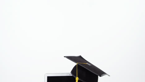 Close-up-of-laptop,-mortar-board-and-stack-of-books