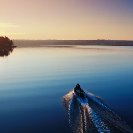 two fishermen in motor boat in the evening. speedboat moving on the water surface at sunset. aerial view.
