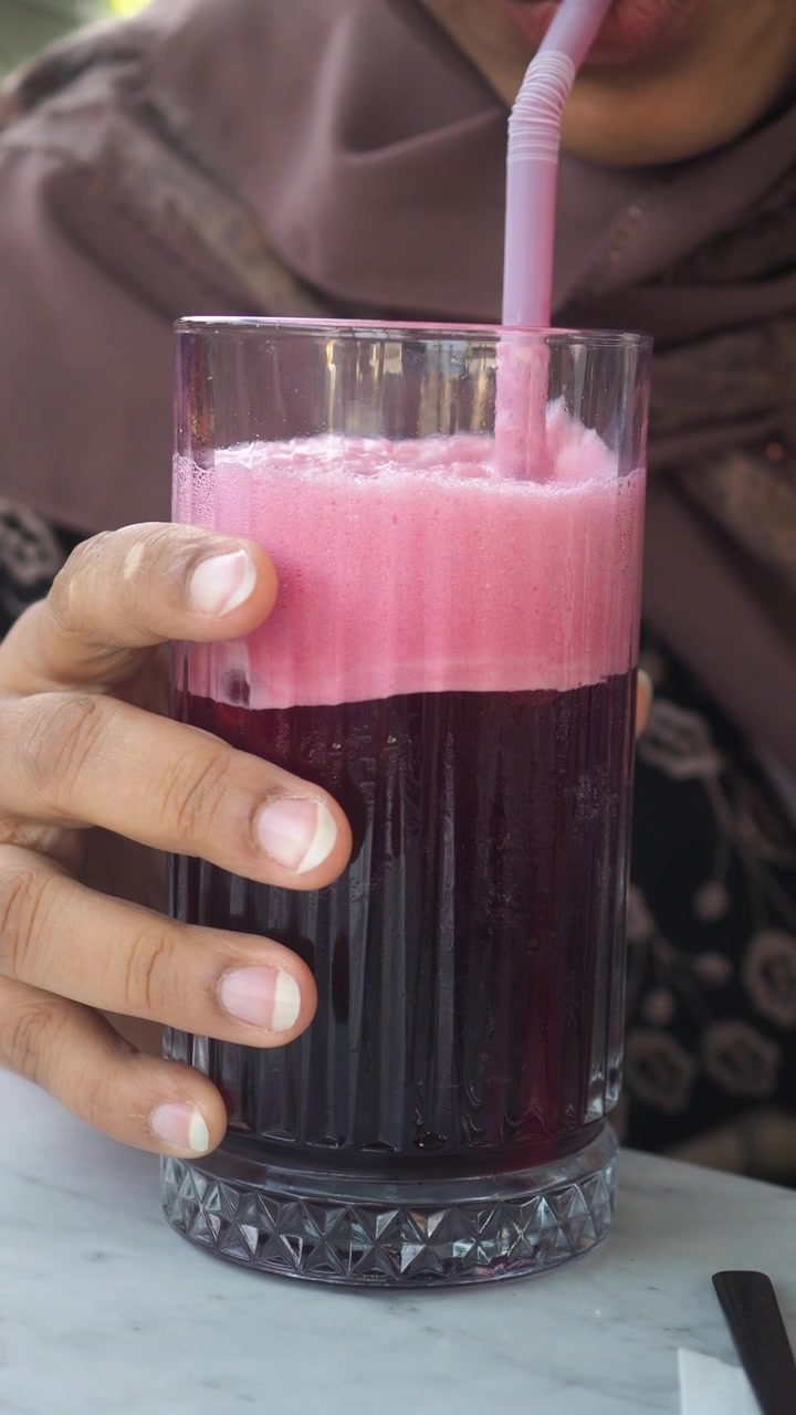 Persona che sorseggia un succo rosso salutare con schiuma rosa attraverso una cannuccia