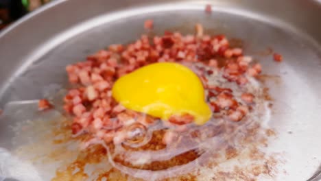 primer plano de la mano rompiendo el huevo en una sartén para acampar con tocino