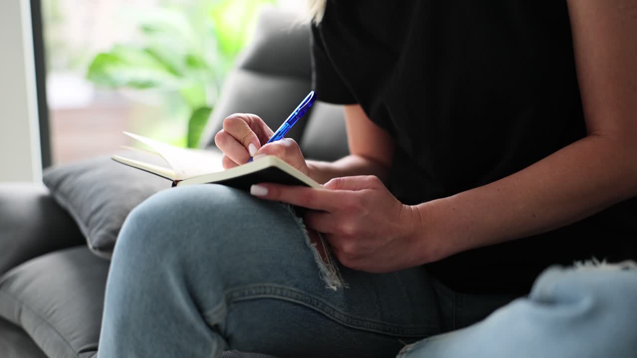 Person Writing in Notebook While Sitting on a Couch