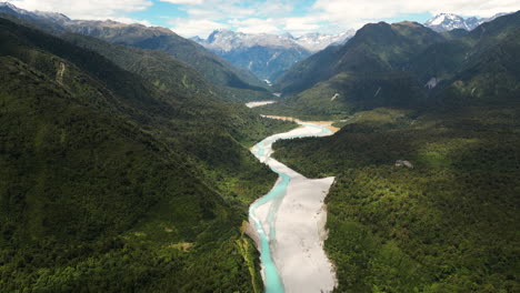 drone flying over incredible valley with turquoise river flowing through it in new zealand