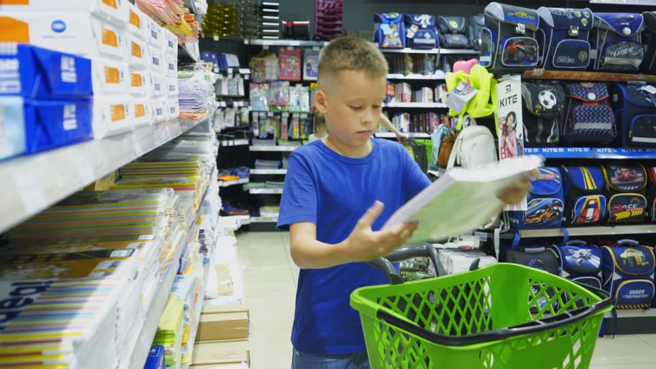 Vinnitsa, Ukraine - August, 2018: Cute child choosing school stationery in store. Many colorful tools and supplies on the shelf of a stationery shop