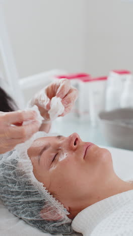 cosmetólogo médico limpia la cara y los ojos de la mujer procedimiento de limpieza con toallitas de algodón en la clínica de belleza