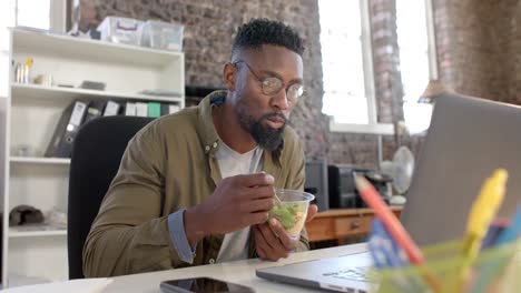 Konzentrierter-Afroamerikanischer-Gelegenheitsgeschäftsmann-Benutzt-Laptop-Und-Isst-Im-Büro-In-Zeitlupe-Zu-Mittag