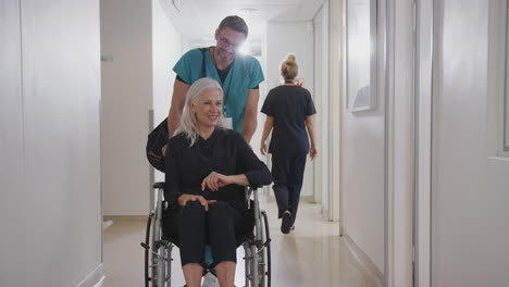 Un-Ordenanza-Masculina-Empujando-A-Una-Paciente-Mayor-Siendo-Dada-De-Alta-Del-Hospital-En-Silla-De-Ruedas