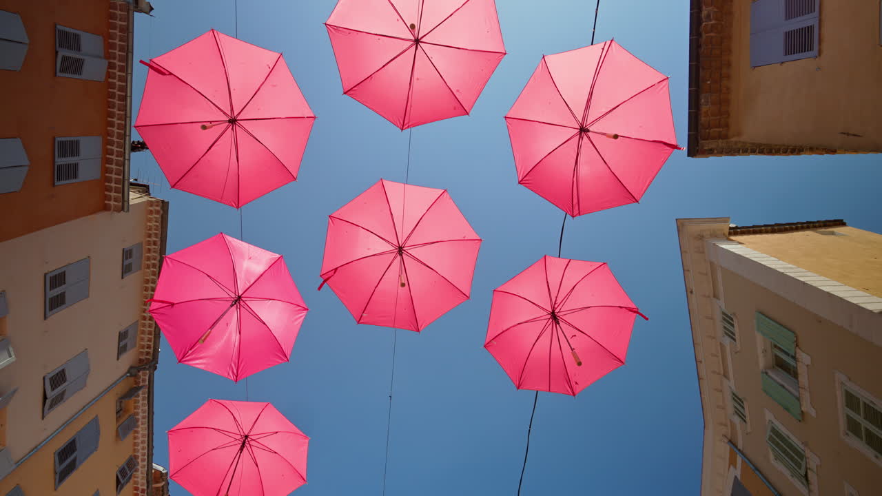 Rows of pink umbrellas above the streets of the old town in Grasse, France with the blue sky on the background