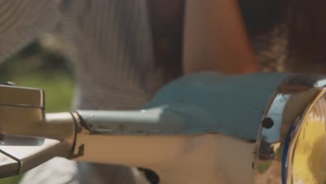 Close-up-of-a-indian-woman-hands-on-a-light-blue-vespa-handlebar,-wearing-a-summer-dress,-on-a-sunny-day