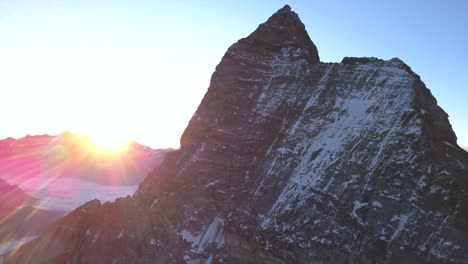 Beautiful-sunrise-over-distant-mountain-ridge-with-famous-pyramid-shaped-peak-of-Matterhorn,-Monte-Cervino,-Mont-Cervin,-in-foreground-with-steep-rocky-cliff-faces-and-light-snow